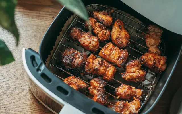 Air fryer aberta com o cesto cheio de alimentos dourados, sobre mesa de madeira