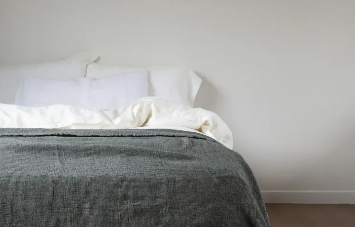 Cama arrumada com colchão claro e manta cinza em quarto minimalista