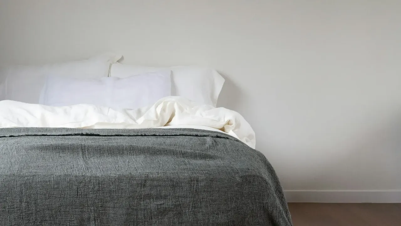 Cama arrumada com colchão claro e manta cinza em quarto minimalista