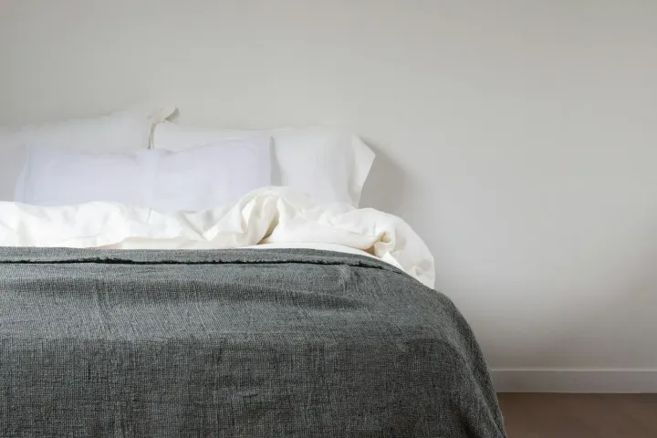 Cama arrumada com colchão claro e manta cinza em quarto minimalista