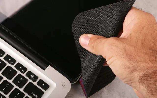 Mão passando pano de microfibra na tela de um notebook