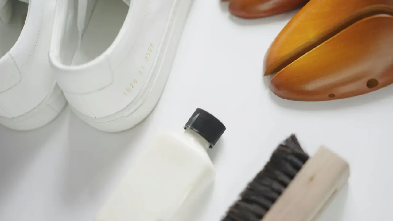 Tênis brancos ao lado de escova e produto de limpeza