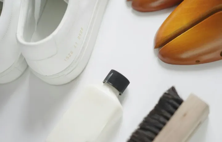 Tênis brancos ao lado de escova e produto de limpeza