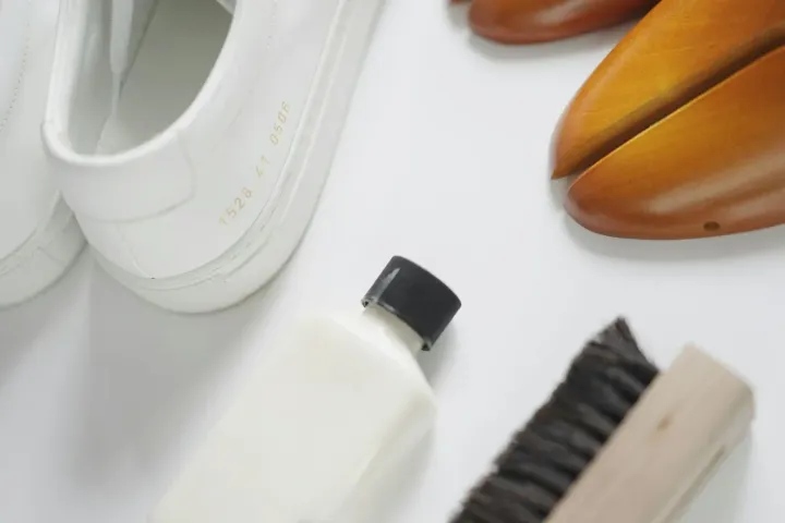 Tênis brancos ao lado de escova e produto de limpeza