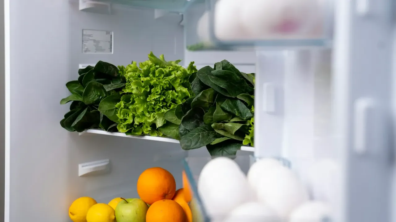 Geladeira aberta organizada com folhas verdes, frutas e ovos