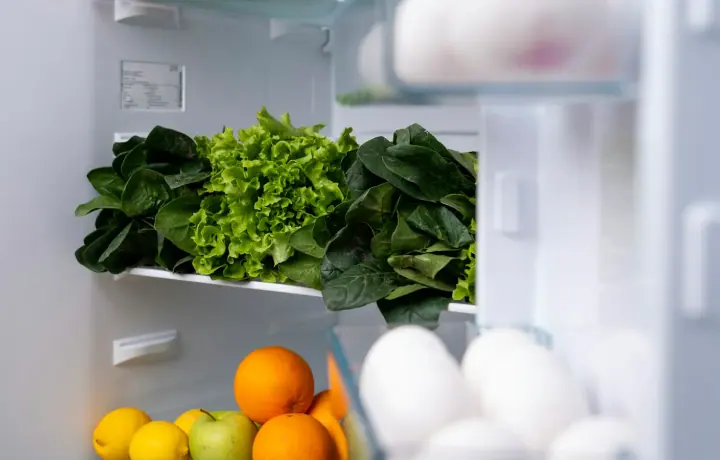 Geladeira aberta organizada com folhas verdes, frutas e ovos
